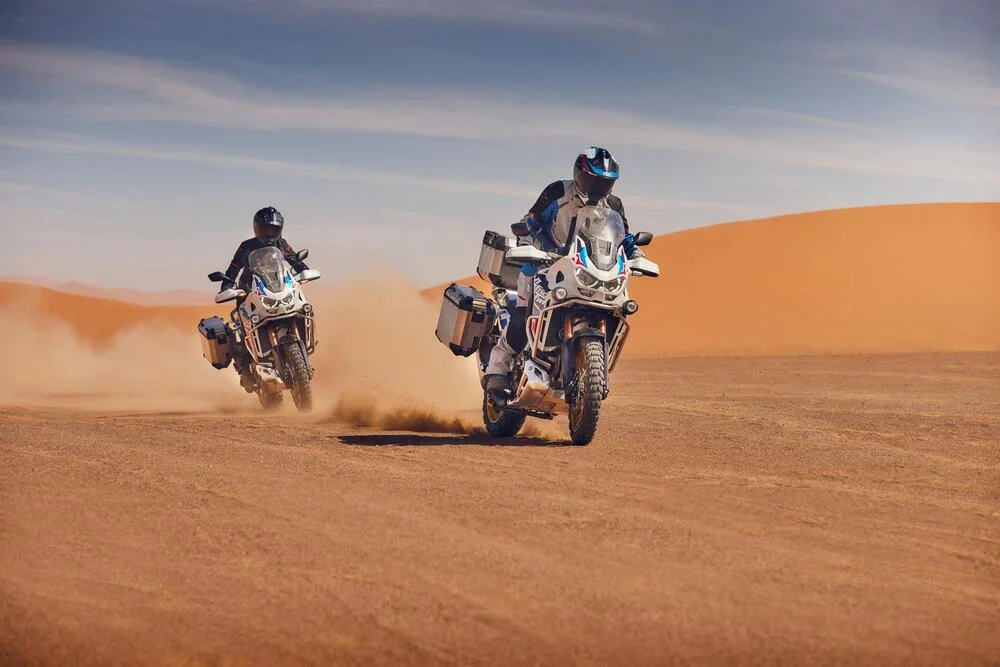 Dois pilotos testando a CRF1100L Africa Twin 2024 cada um no deserto.
